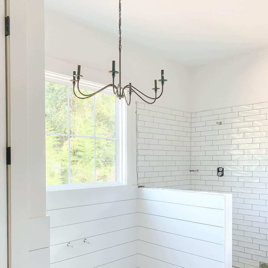 Black candelabra fixture suspended in a white bathroom with subway tile and shiplap walls.