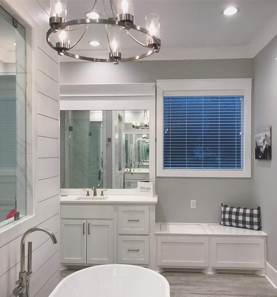 Wheel-inspired chandelier above a white freestanding tub and built-in bench in a bright shiplap bathroom.