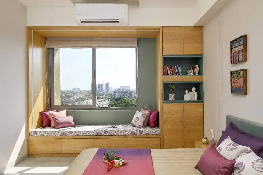 Bedroom with a built-in window nook, wooden storage bench, soft cushions, and bookshelves for a cozy and functional sitting area.