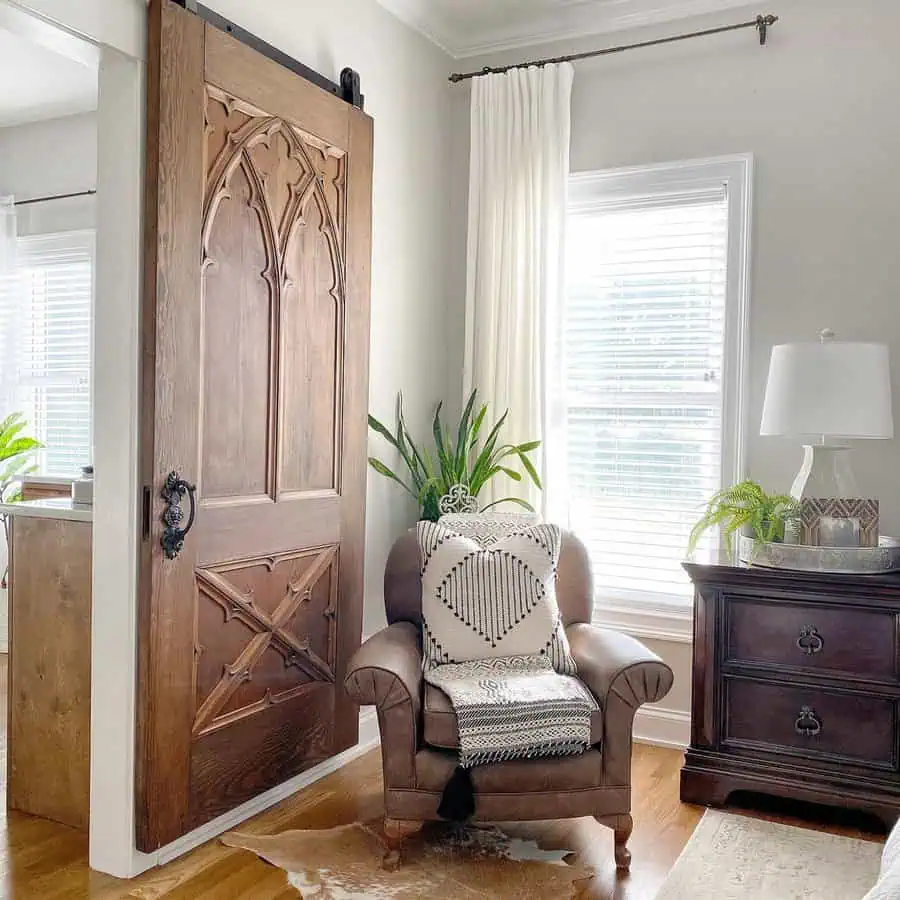 Bedroom sitting area with a leather armchair, rustic sliding barn door, textured textiles, and greenery for a warm and inviting space.