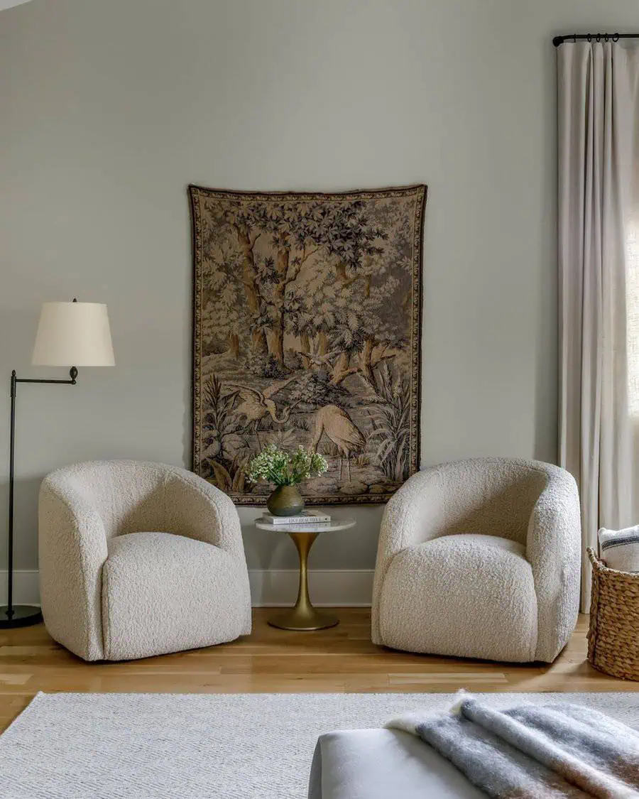Bedroom sitting area with two boucle chairs, a gold side table, a decorative tapestry, and soft neutral tones for a cozy and elegant look.