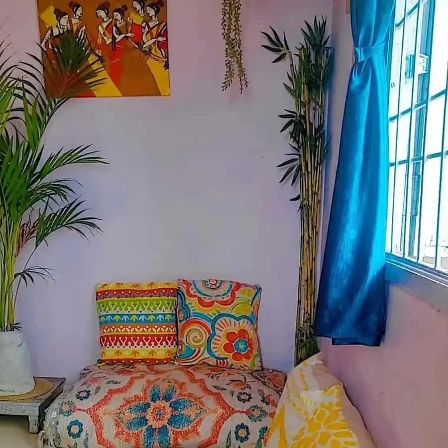 Boho-style bedroom sitting area with colorful cushions, a patterned throw, lush plants, and cultural artwork for a lively, cozy look.