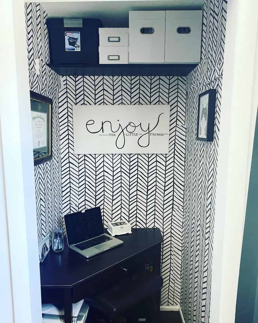 Closet office with herringbone wallpaper, shelf storage, and motivational decor for a bold, compact workspace.