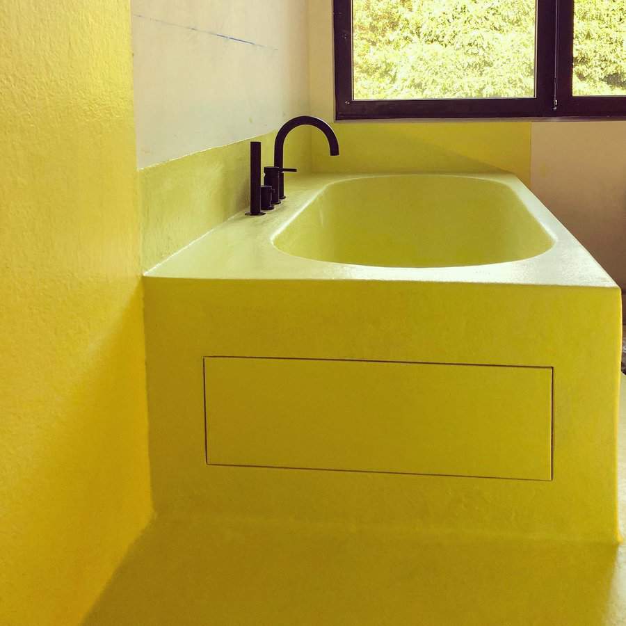 Yellow bathtub with black faucet in a minimalist bathroom with large window and modern design.