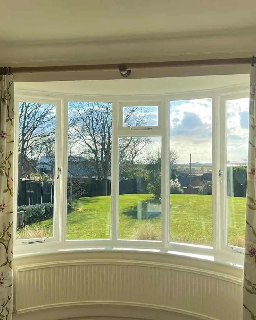 Curved boow window overlooking a green yard and blue sky, framed by floral curtains.