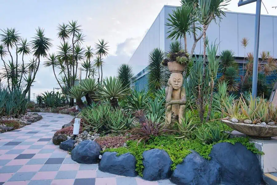 Garden with a central stone sculpture, tall yucca plants, and a colorfully tiled path creating a vibrant desert-inspired setting.