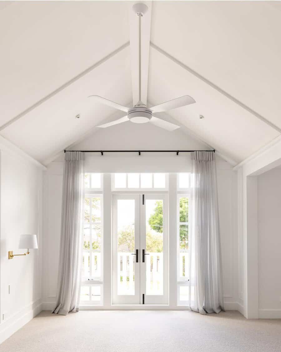 White vaulted room with a large ceiling fan, tall doors, and sheer drapes allowing plenty of natural light.