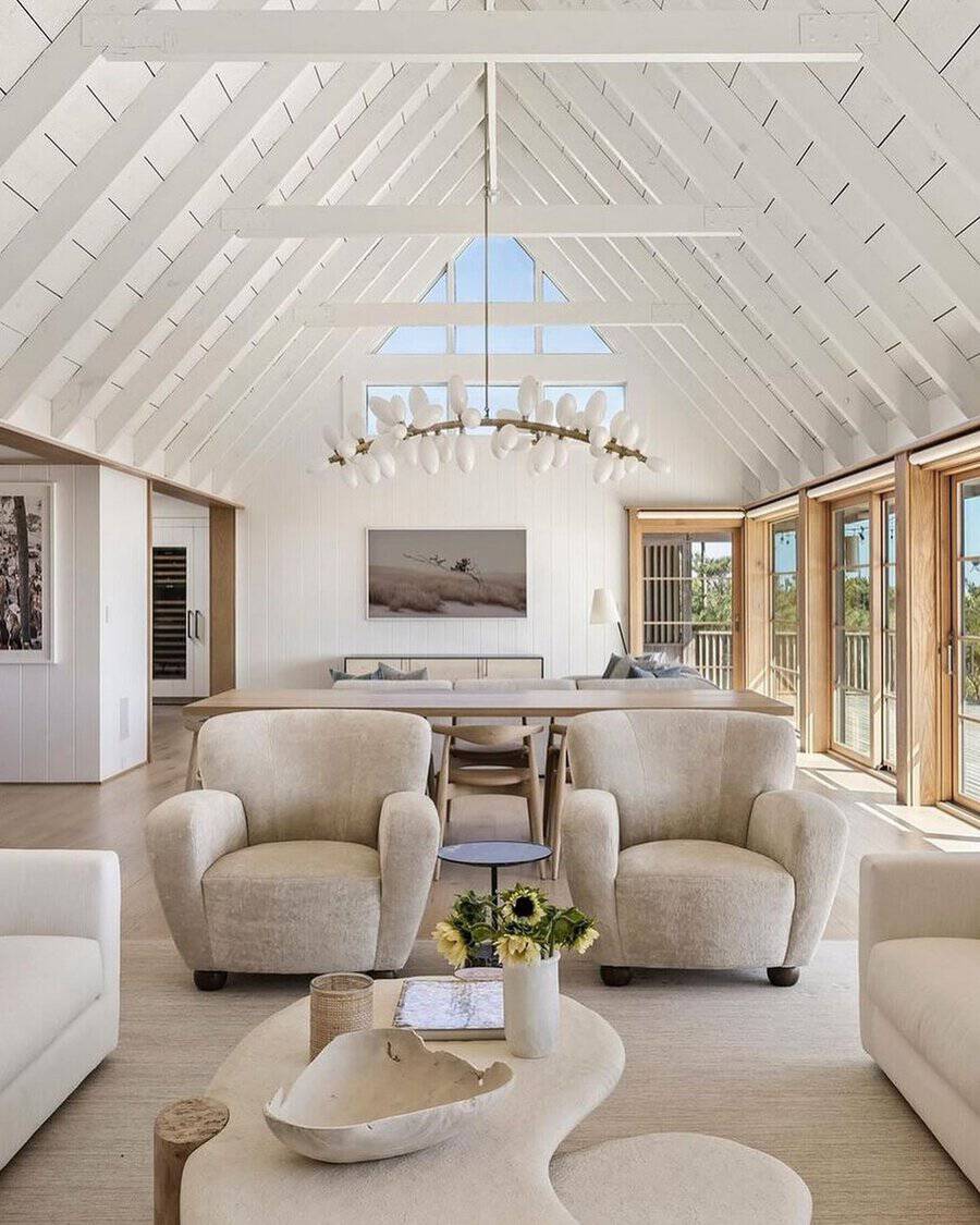 White vaulted living room with a whimsical bubble-like chandelier, plush chairs, and large windows flooding the space with light.