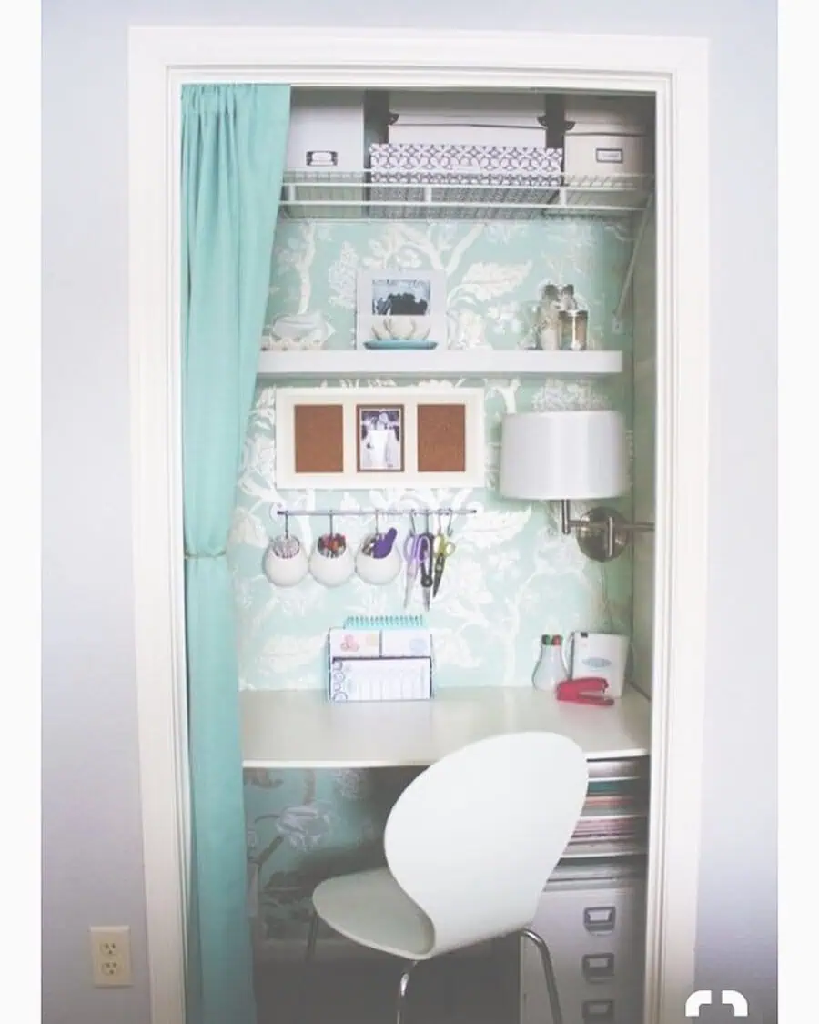 Closet office with blue and white wallpaper, floating shelves, a white desk, a hanging organizer, a mounted lamp, and a curtain for privacy.