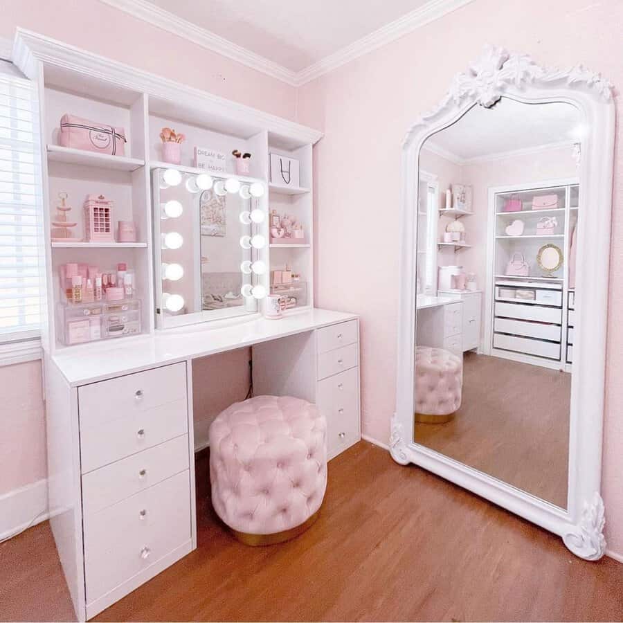 White vanity with a Hollywood mirror, pink tufted stool, and built-in storage for a stylish and organized pink bedroom.
