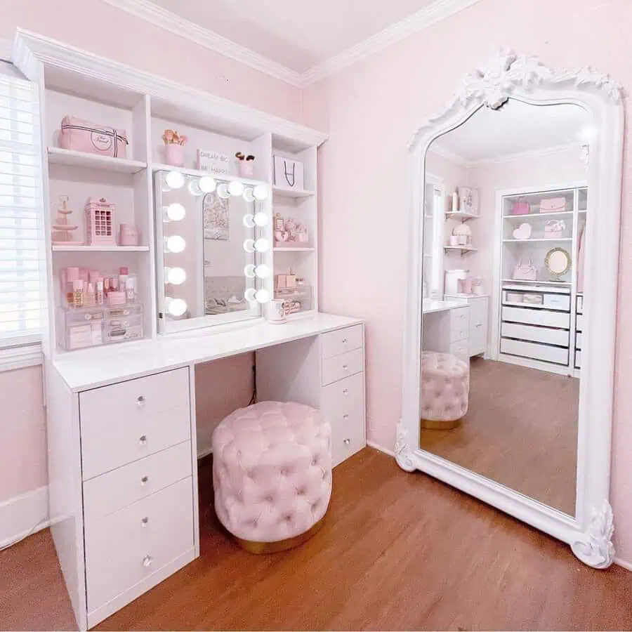 White vanity with a Hollywood mirror, pink tufted stool, and built-in storage for a stylish and organized pink bedroom.