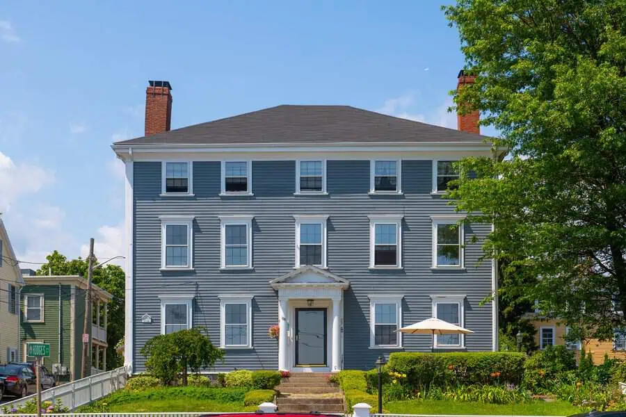Blue Colonial Georgian house with central entry pediment, symmetrical windows, and twin chimneys against a clear sky.
