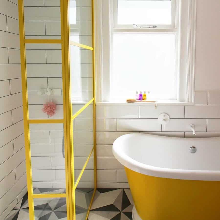Bathroom featuring a yellow bathtub, a yellow-framed shower, white subway tile, and geometric flooring.