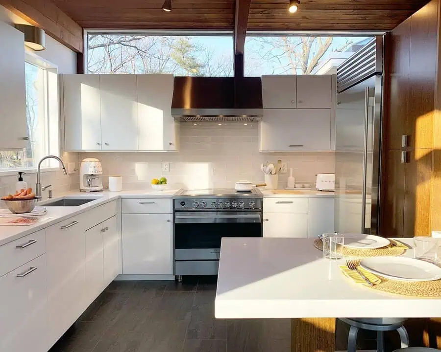 White mid-century kitchen with a clerestory window, wood ceiling, subway tile backsplash, and stainless appliances.