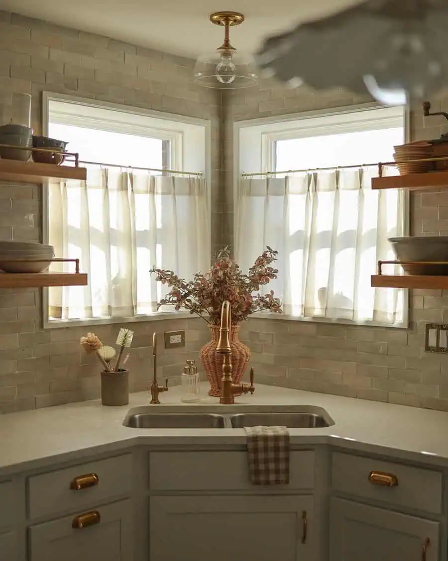 Corner sink with linen curtains, warm brass fixtures, and soft brick tile in a cozy, rustic-modern kitchen.