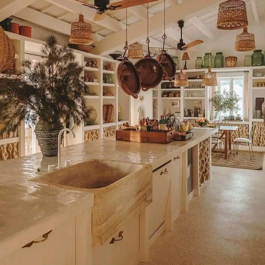 Modern Spanish kitchen with white cabinetry, terracotta flooring, exposed wood beams, a patterned island, and industrial pendant lighting.