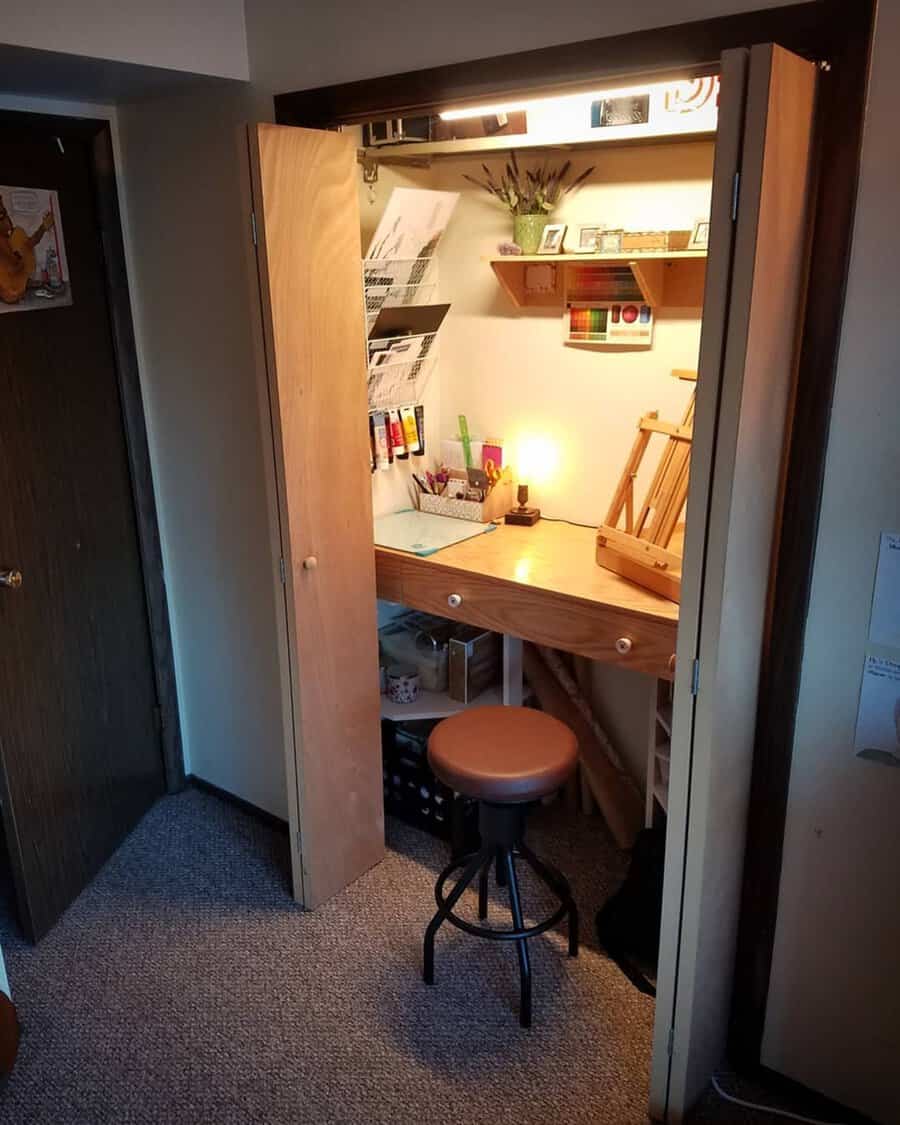 Closet converted into a small, tidy office nook with a wooden desk, art supplies, and warm lighting for a comfy workspace.