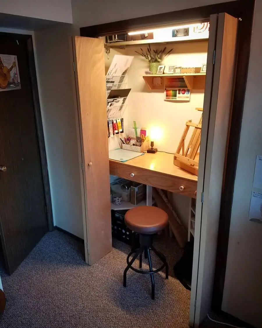 Closet converted into a small, tidy office nook with a wooden desk, art supplies, and warm lighting for a comfy workspace.