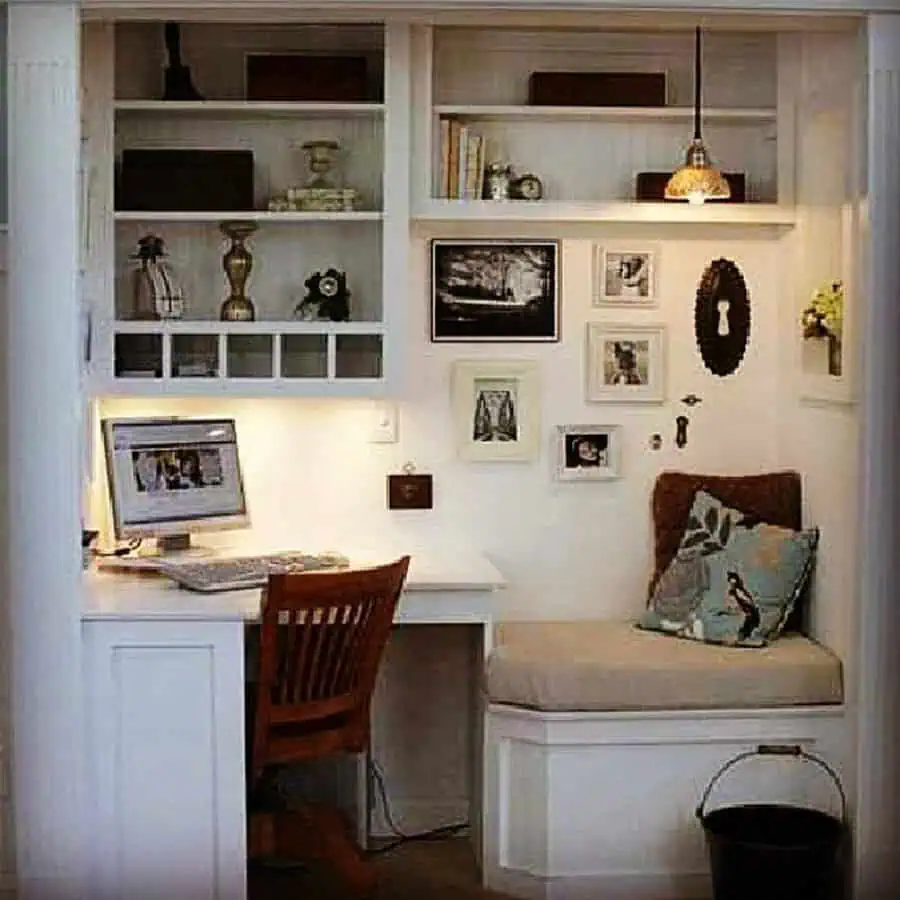 Closet office with built-in desk, open shelving, cozy bench seating, framed artwork, warm lighting, and vintage-inspired decor.