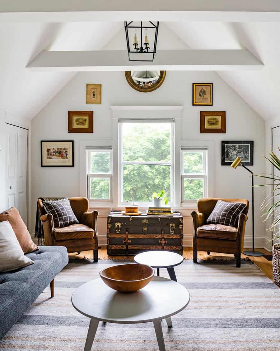 White vaulted living room with leather chairs, a vintage trunk coffee table, and modern accents under a lantern-style pendant.