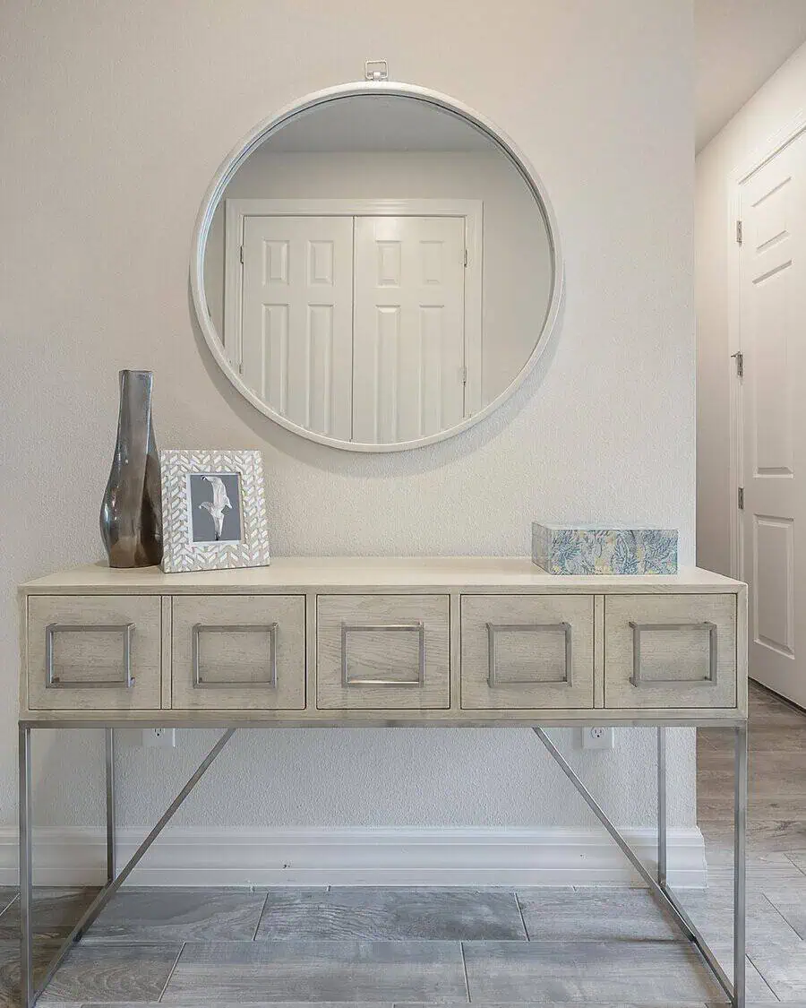 Round mirror above a minimalist console table with a vase, picture frame, and decorative box in a light-colored entryway.