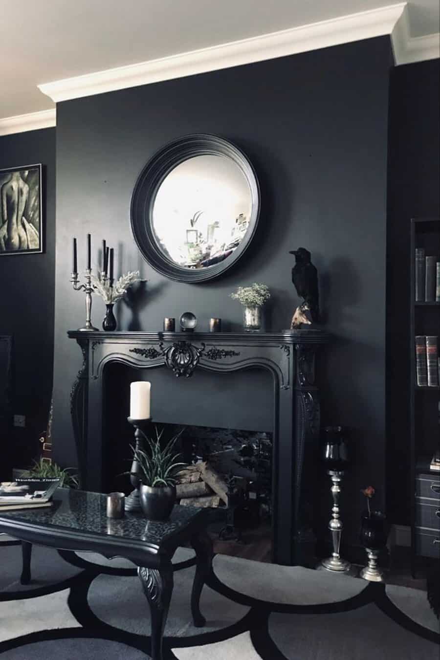 Round mirror above a black fireplace with candles, a raven statue, and a dark-toned coffee table in a stylish, moody living room.