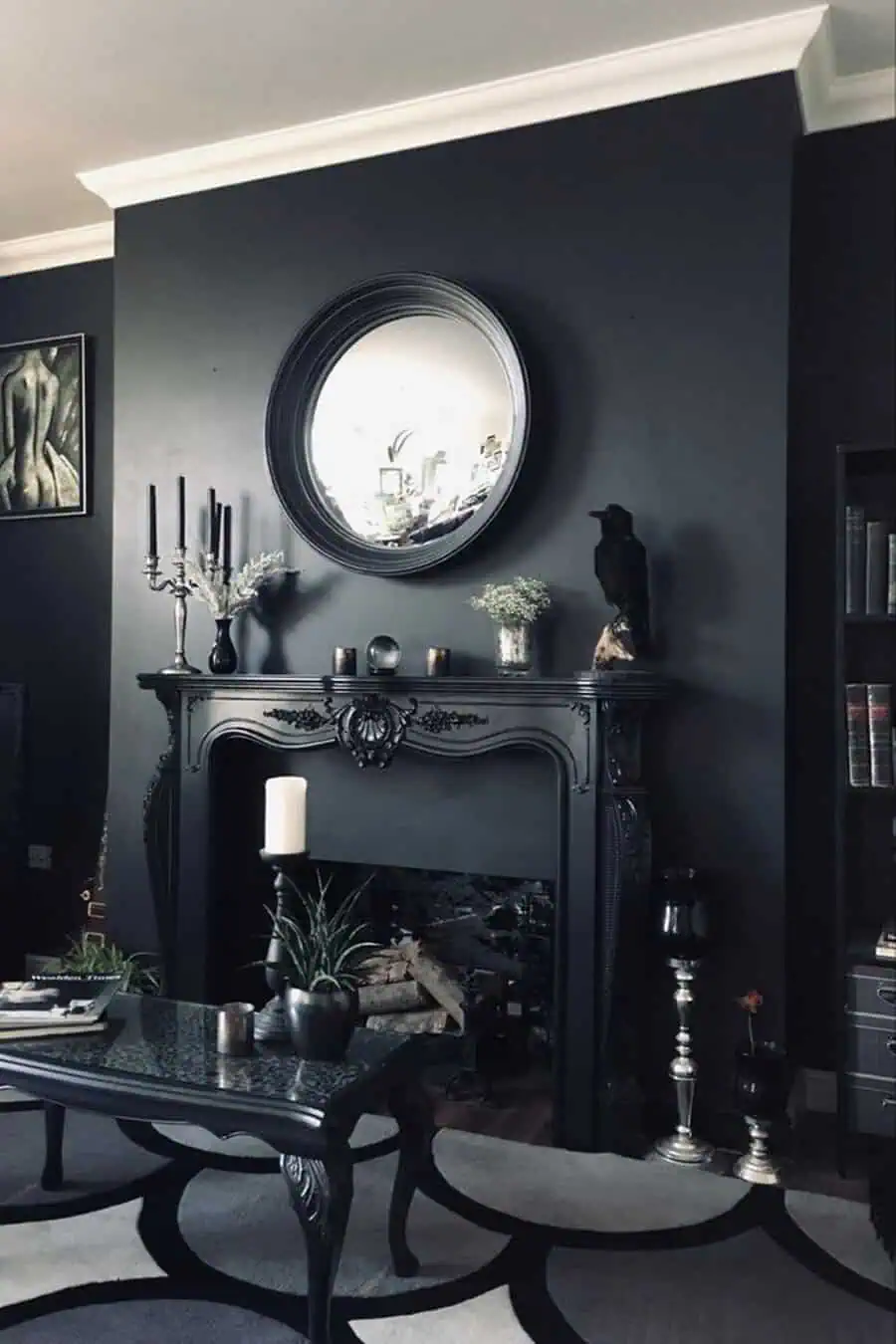 Round mirror above a black fireplace with candles, a raven statue, and a dark-toned coffee table in a stylish, moody living room.