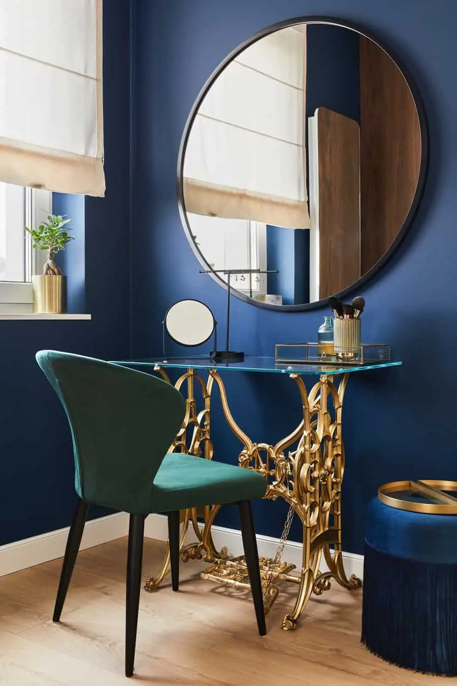 Large round mirror above a gold vanity table with a green chair and beauty accessories in a stylish blue room.