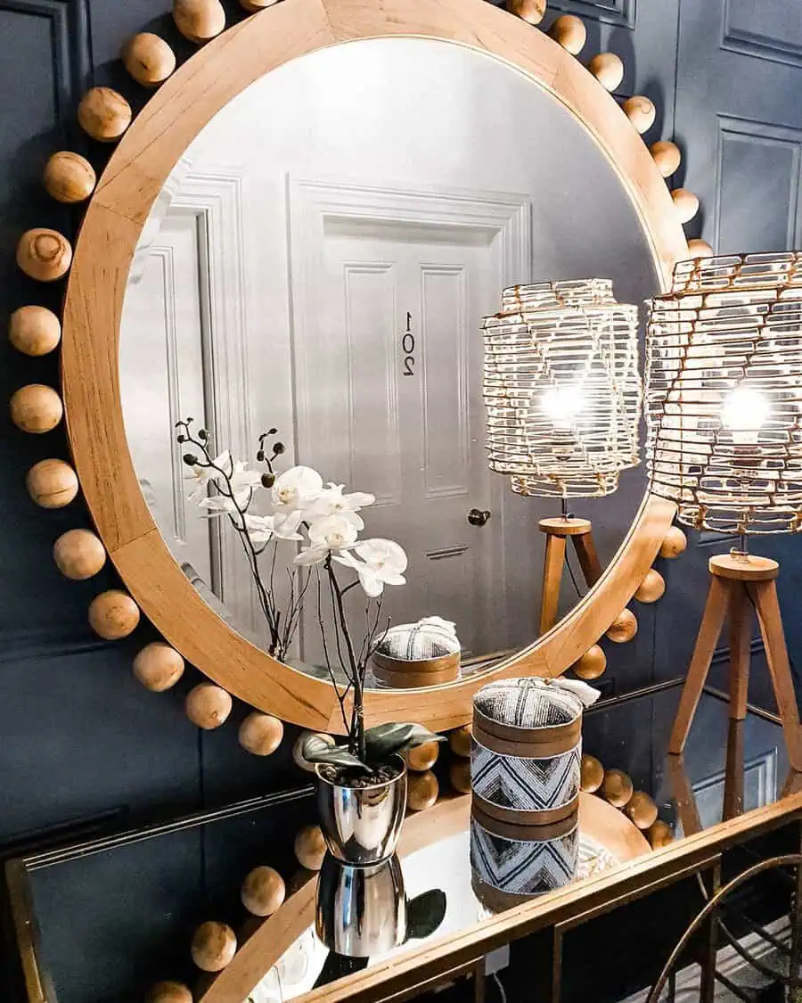 Large wooden-framed mirror with rounded details above a table, accented by orchids and stylish lighting.
