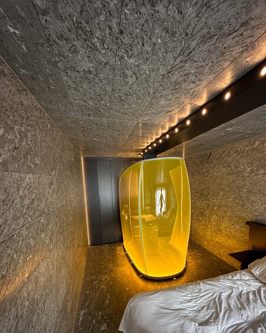 Futuristic bedroom with a bright yellow shower pod, stone walls, dark cabinets, and subtle LED accents.