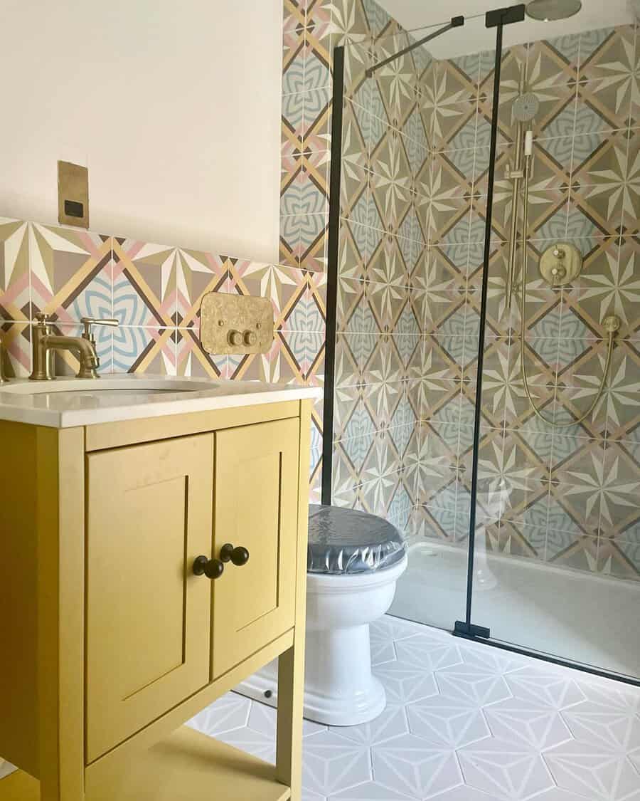 Bathroom with geometric pastel tiles, mustard vanity, gold fixtures, and a modern glass shower for a stylish, contemporary feel.