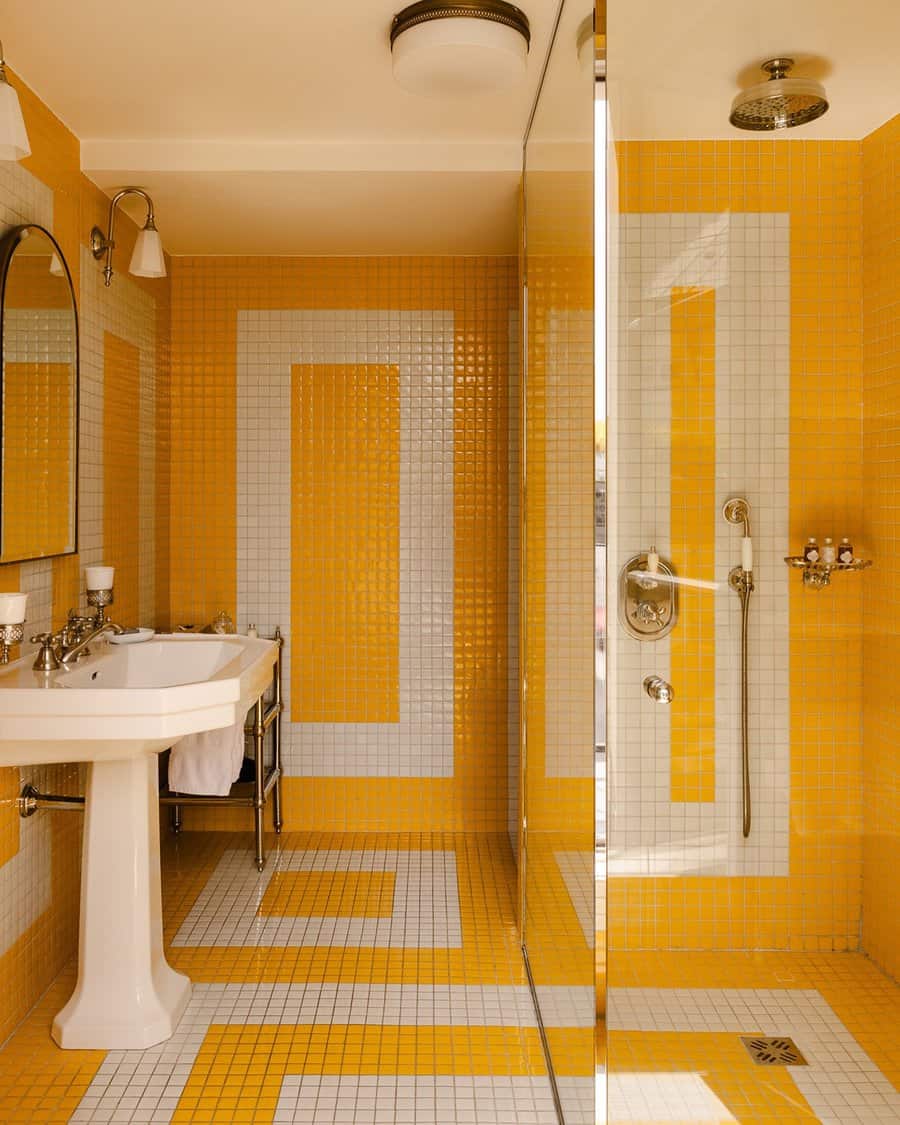 Bathroom with bold yellow and white geometric tiles, a pedestal sink, modern shower, and frameless glass partition for a vibrant, clean look.