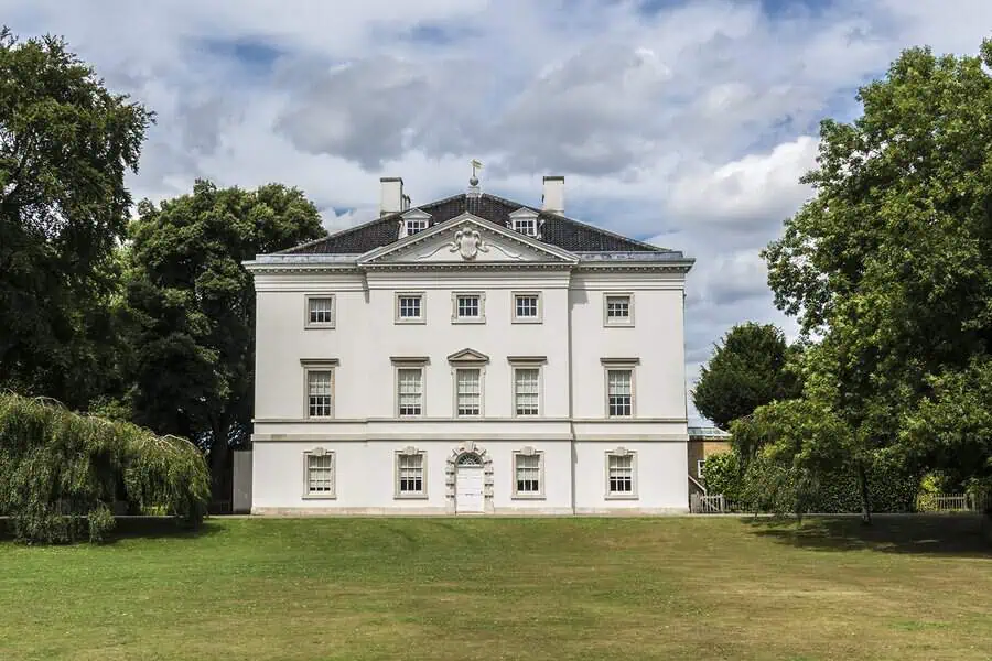 Stately British Georgian manor in white with symmetrical windows and a prominent pediment on a green lawn.