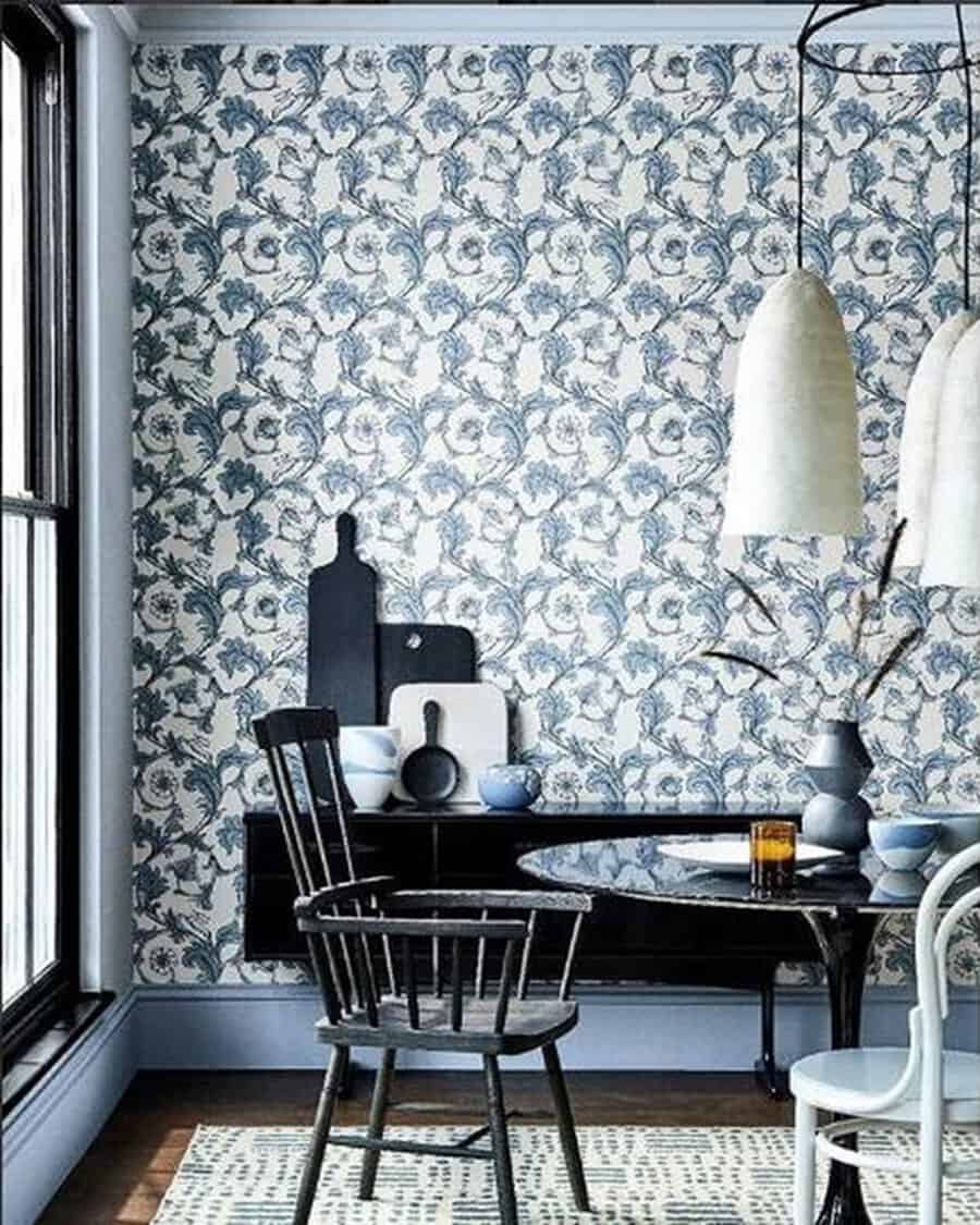 Blue-and-white floral wallpaper covering a wall, paired with dark wood furnishings and simple decor in a light-filled space.