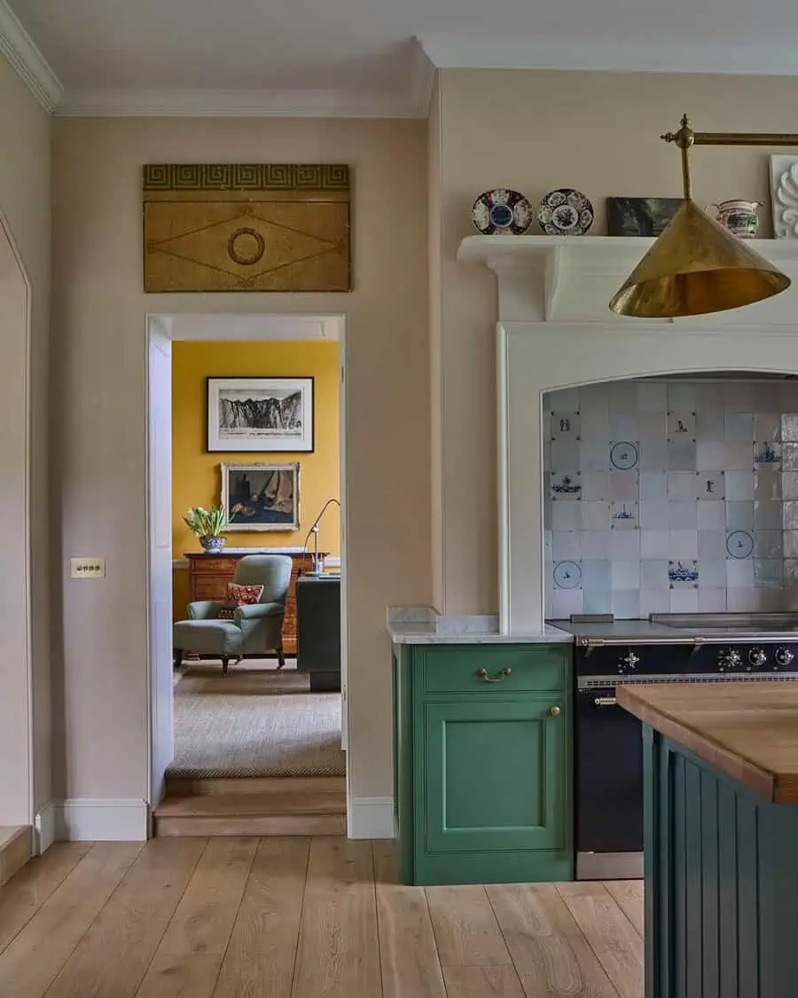 Georgian-style kitchen with green cabinets, brass accents, a tiled backsplash, and a bright yellow sitting room in view.