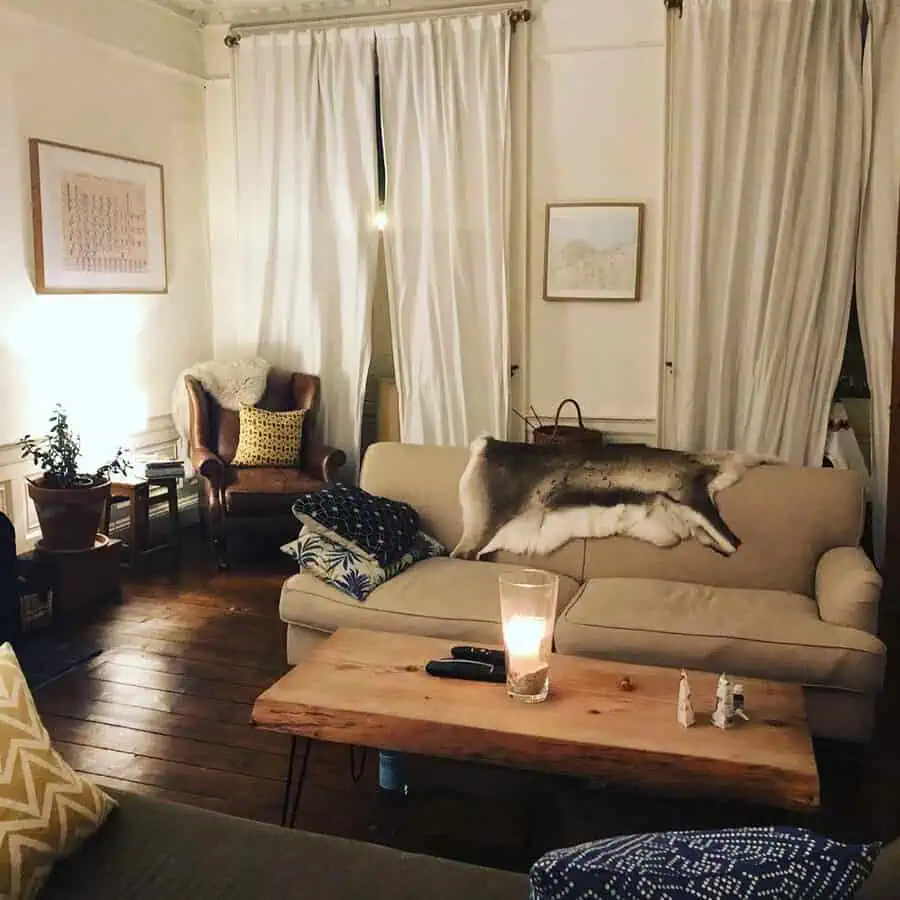 Comfortable living room with white drapes, a leather armchair, wood floor, and soft furnishings evoking a mild Georgian touch.