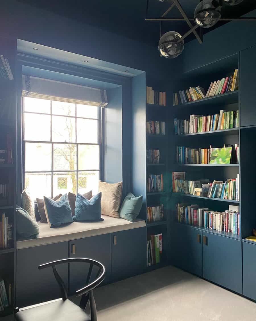 Cozy reading nook with built-in shelves, blue walls, a comfy window seat, and soft lighting for a perfect reading space.