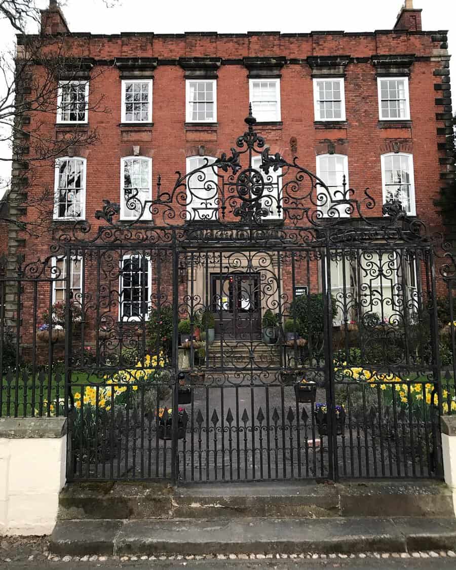 Intricate wrought-iron gate featuring elaborate scrollwork in front of a red-brick Georgian building.