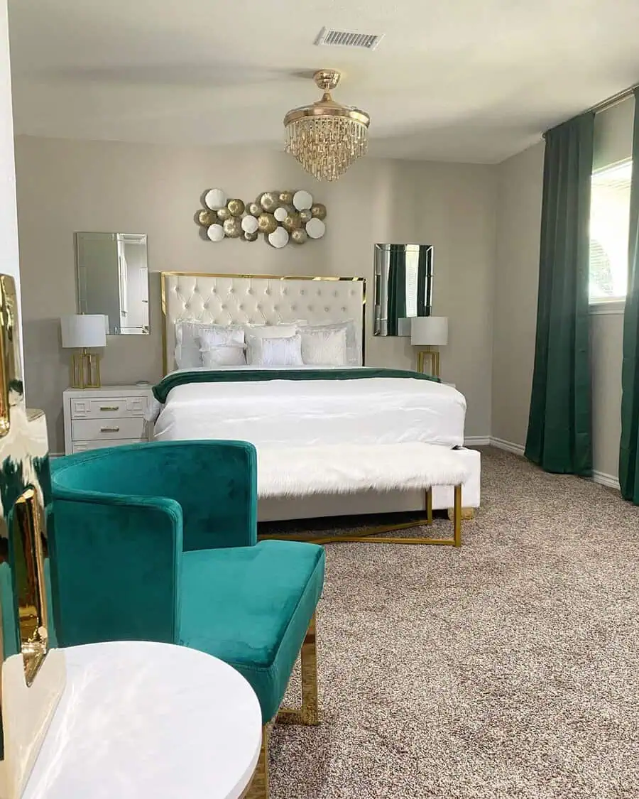 Bedroom sitting area with an emerald green velvet chair, gold accents, plush textiles, and a chandelier for a glamorous look.