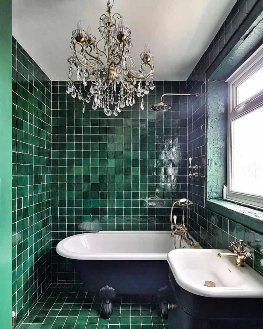 Crystal chandelier in an emerald-tiled bathroom with a black clawfoot tub and matching sink.