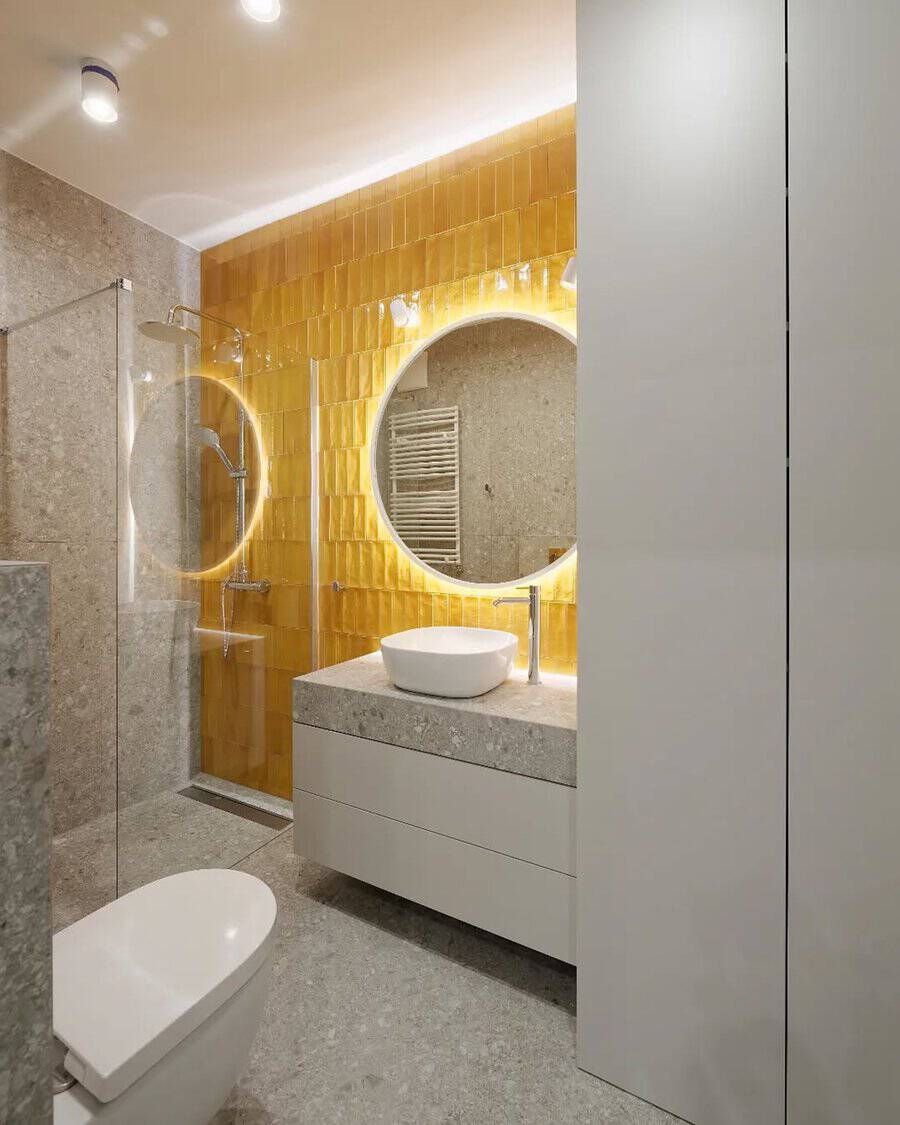 Bathroom with golden glazed tiles, a round backlit mirror, and stone finishes for a modern, eye-catching design.