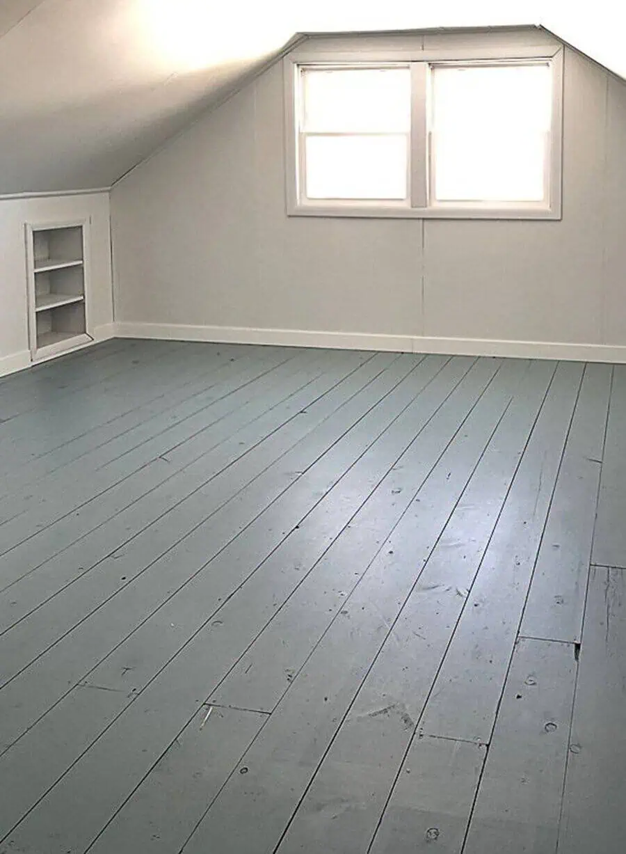 Attic with light gray painted wood floor, neutral walls, and a built-in shelf beneath a window.