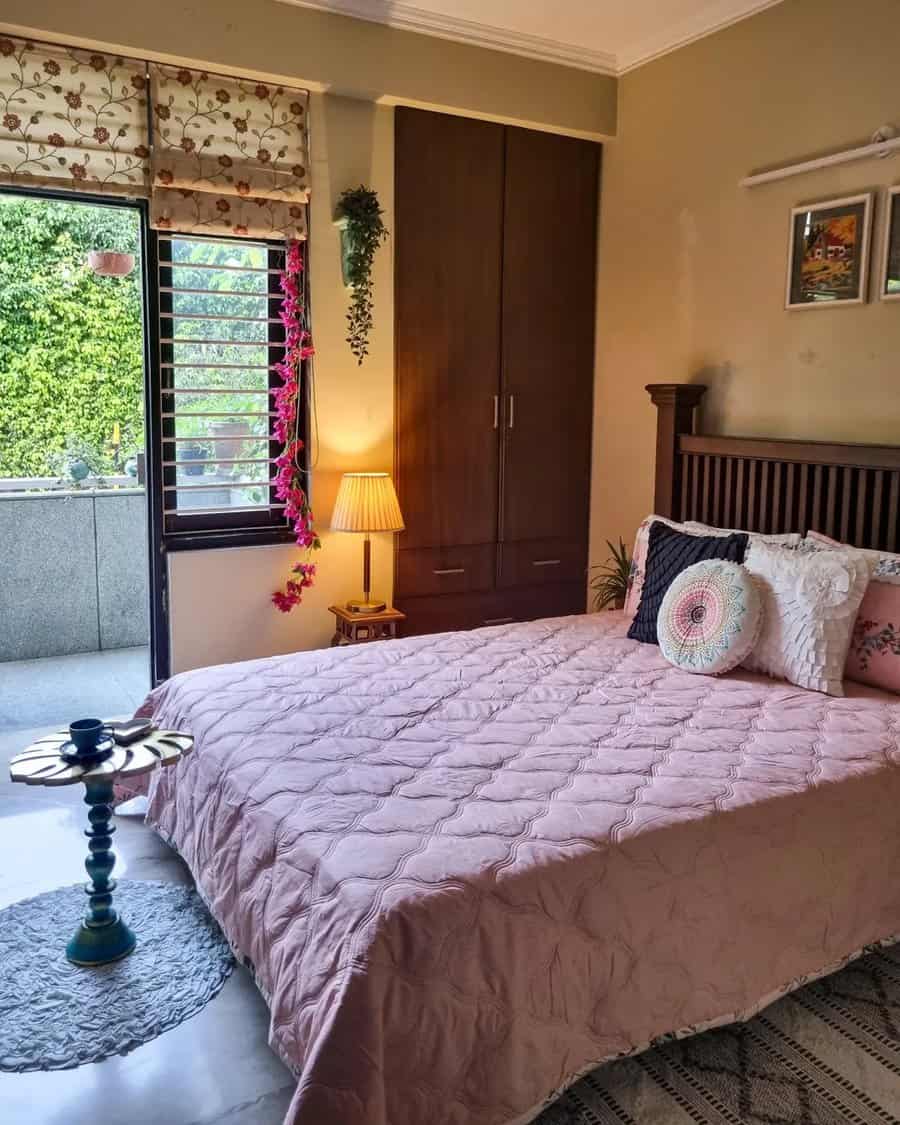 Pink quilted bedspread in a cozy bedroom with wooden furniture, greenery, and layered pillows for a warm, natural ambiance.