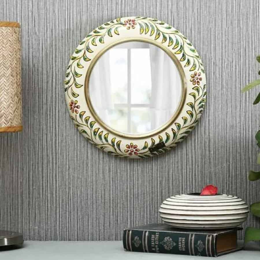 Hand-painted round mirror with floral details on a textured wall, accompanied by stacked books and a small plant.