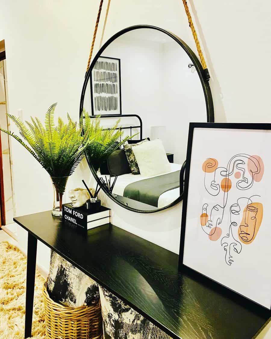 Hanging round mirror with modern decor and stylish accessories above a black console table.