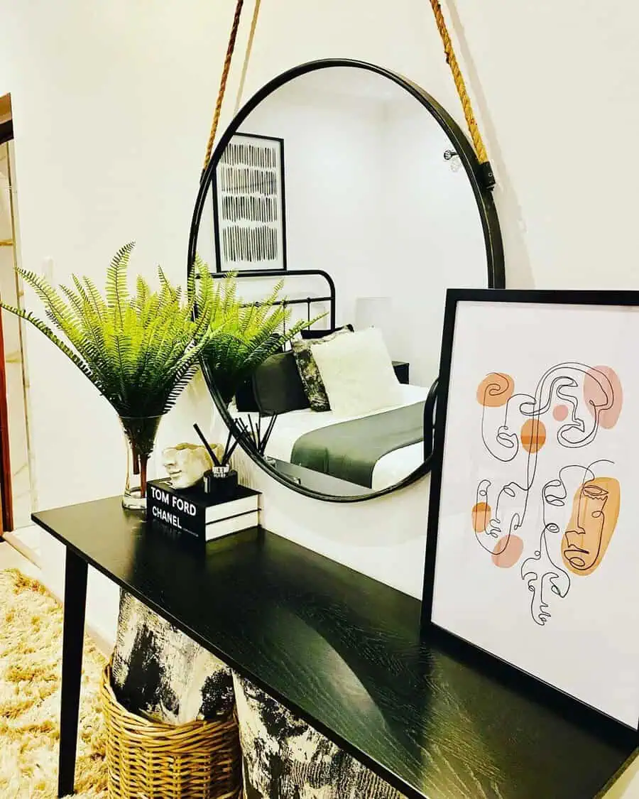 Hanging round mirror with modern decor and stylish accessories above a black console table.