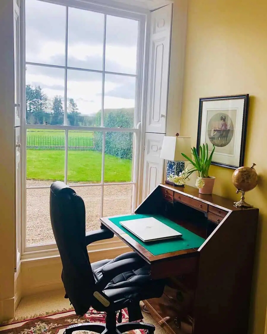 Antique writing desk by a bright window with scenic views, offering a timeless and inspiring workspace.