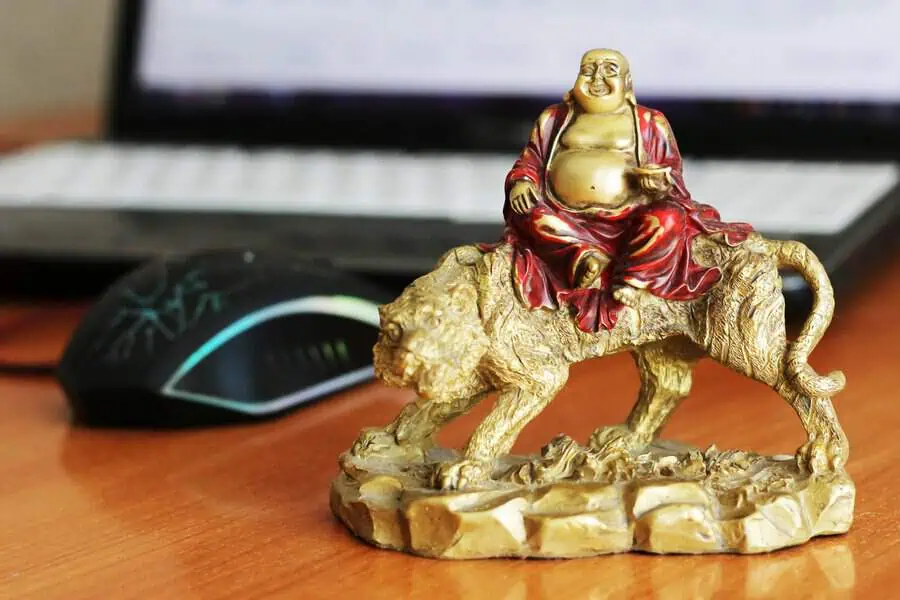 Gold laughing Buddha figure riding a tiger on a wooden desk, bringing prosperity and joy to a home office.