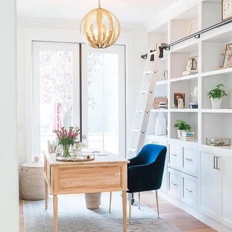 Sunlit home office with built-in shelves, velvet chair, and gold chandelier for a refined, inviting feel.