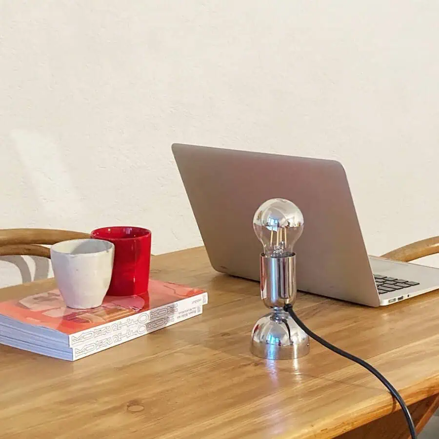 Minimalist desk with a chrome lamp, laptop, and mugs, showcasing a clean, modern workspace.